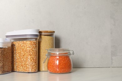 Photo of Different types of cereals and legumes in containers on light marble table, space for text