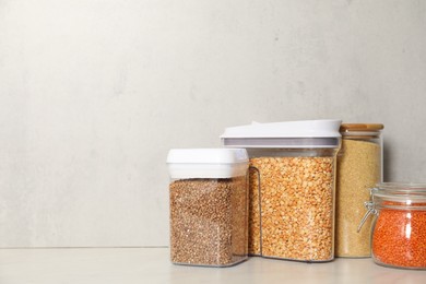 Photo of Different types of cereals and legumes in containers on light marble table, space for text