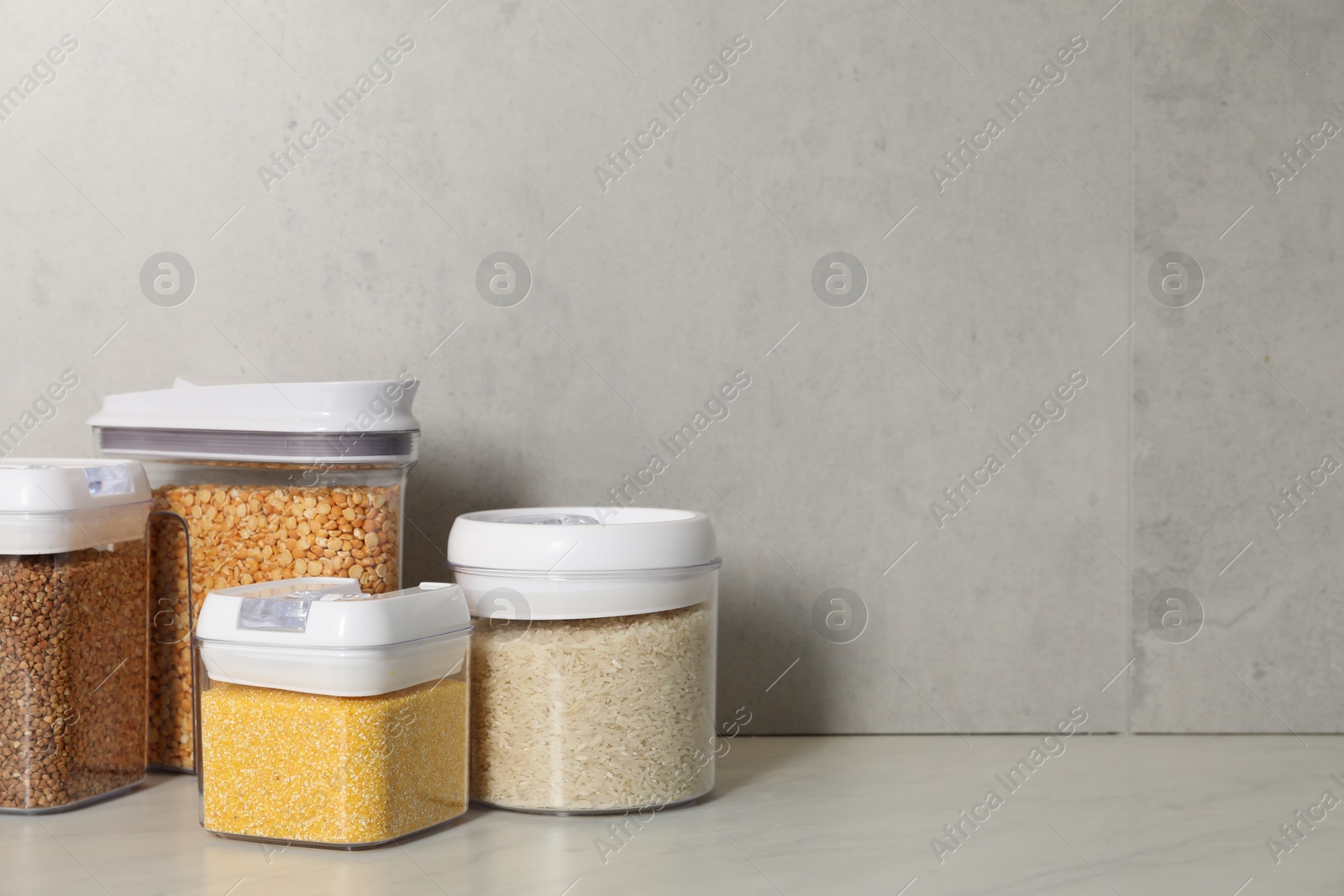 Photo of Different types of cereals in containers on light marble table, space for text