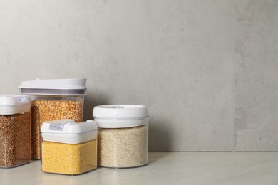 Photo of Different types of cereals in containers on light marble table, space for text