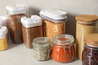 Different types of cereals and legumes in containers on light marble table