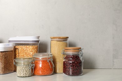 Different types of cereals and legumes in containers on light marble table, space for text