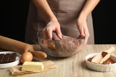 Photo of Woman kneading chocolate dough at wooden table, closeup