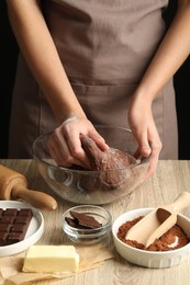 Photo of Woman kneading chocolate dough at wooden table, closeup