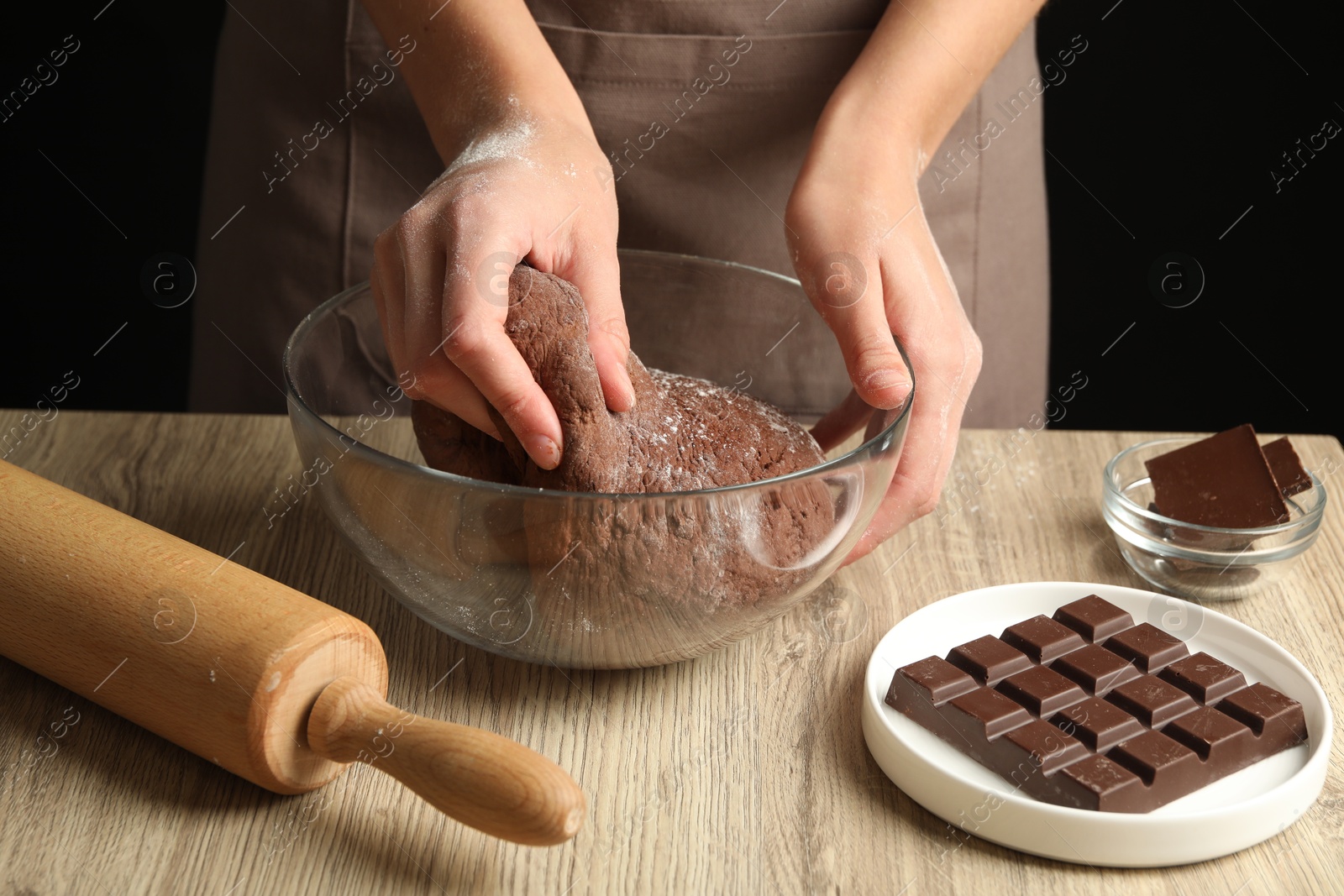 Photo of Woman kneading chocolate dough at wooden table, closeup