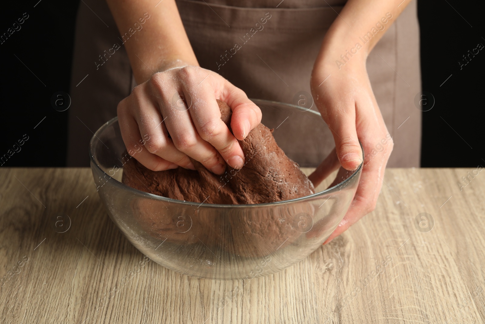 Photo of Woman kneading chocolate dough at wooden table, closeup