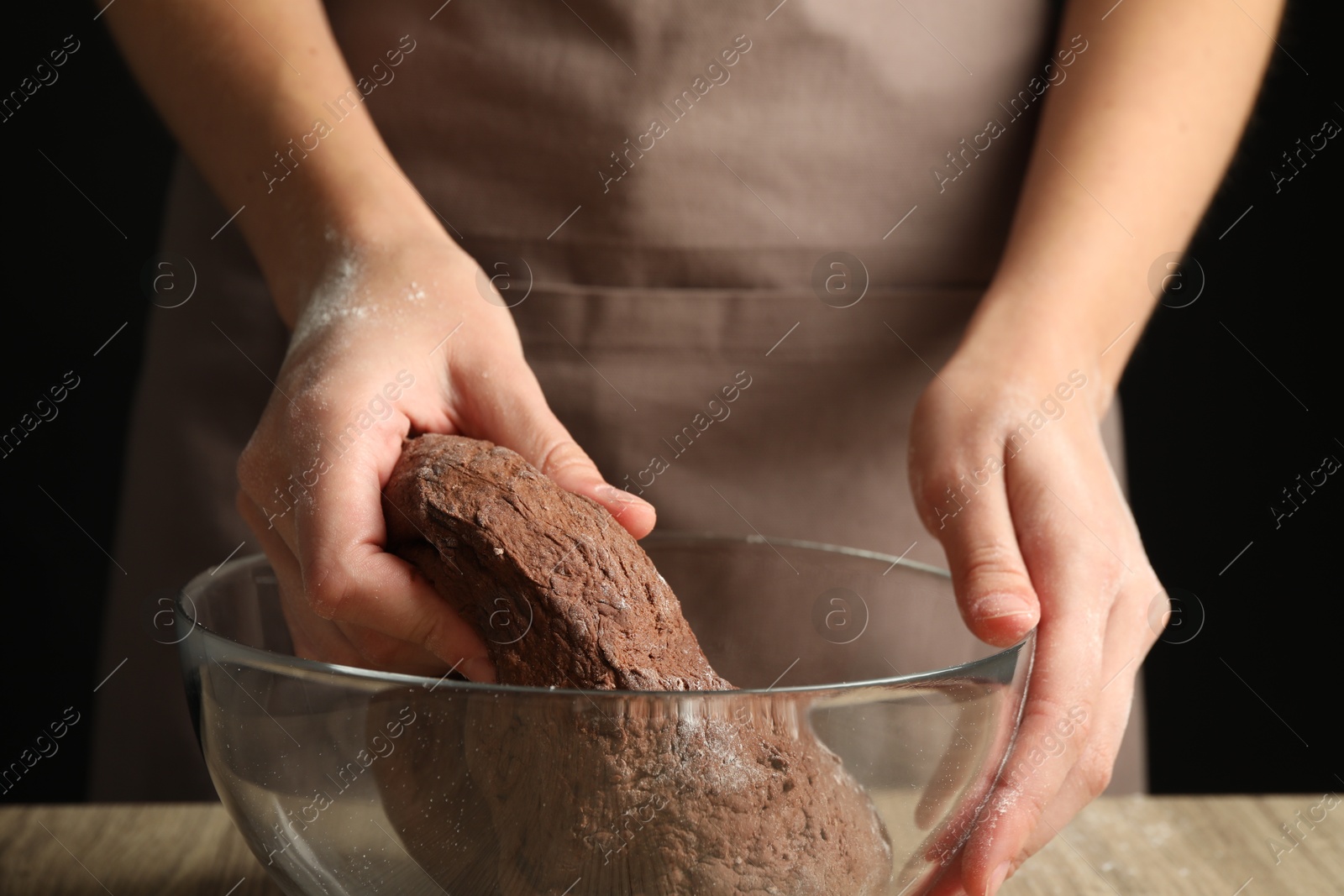 Photo of Woman kneading chocolate dough at wooden table, closeup