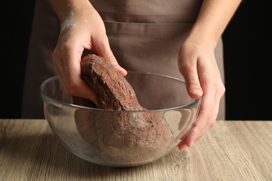 Photo of Woman kneading chocolate dough at wooden table, closeup