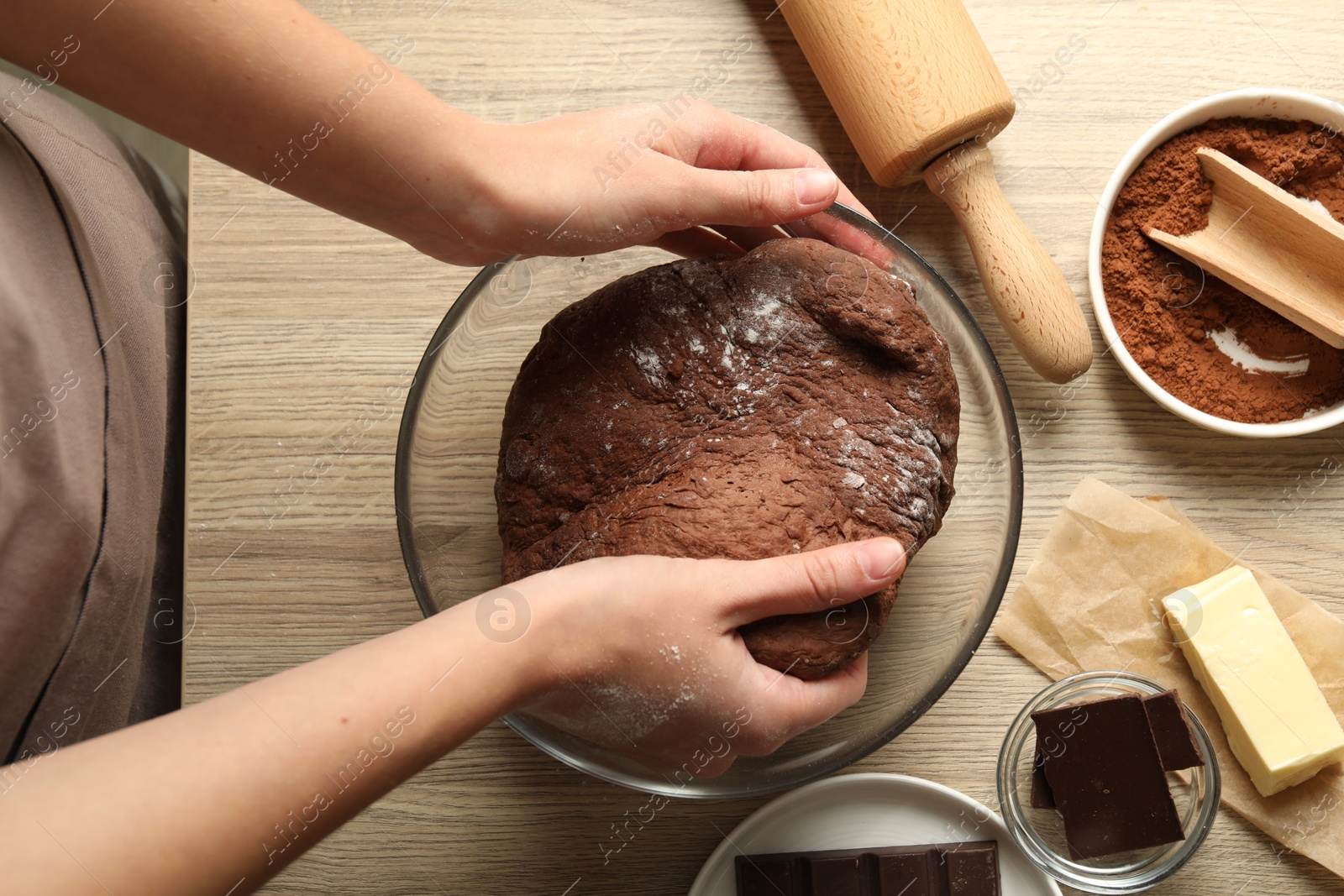 Photo of Woman kneading chocolate dough at wooden table, top view