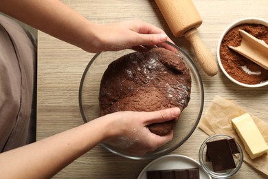 Photo of Woman kneading chocolate dough at wooden table, top view