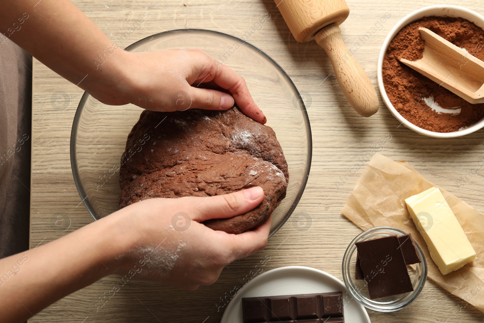 Photo of Woman kneading chocolate dough at wooden table, top view