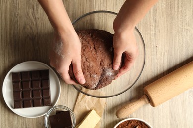 Photo of Woman kneading chocolate dough at wooden table, top view