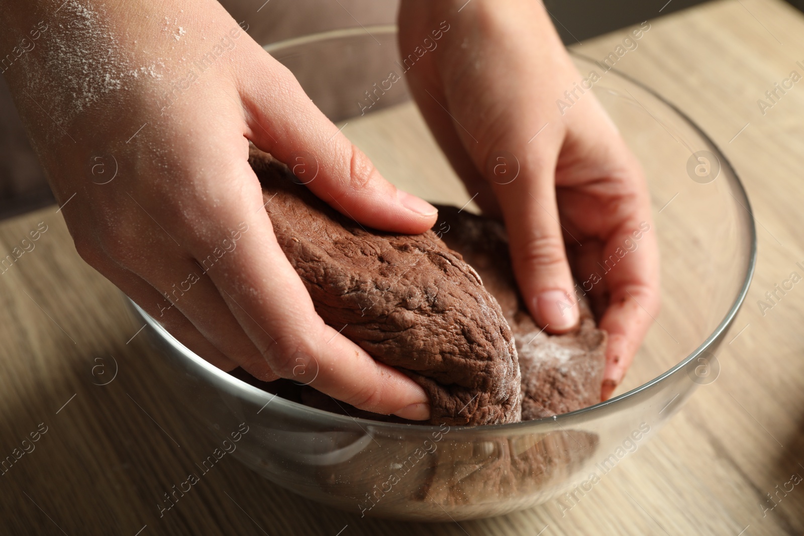 Photo of Woman kneading chocolate dough at wooden table, closeup