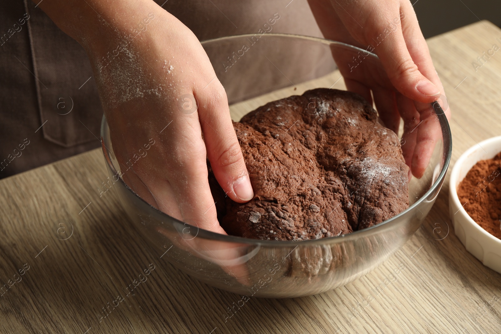 Photo of Woman kneading chocolate dough at wooden table, closeup