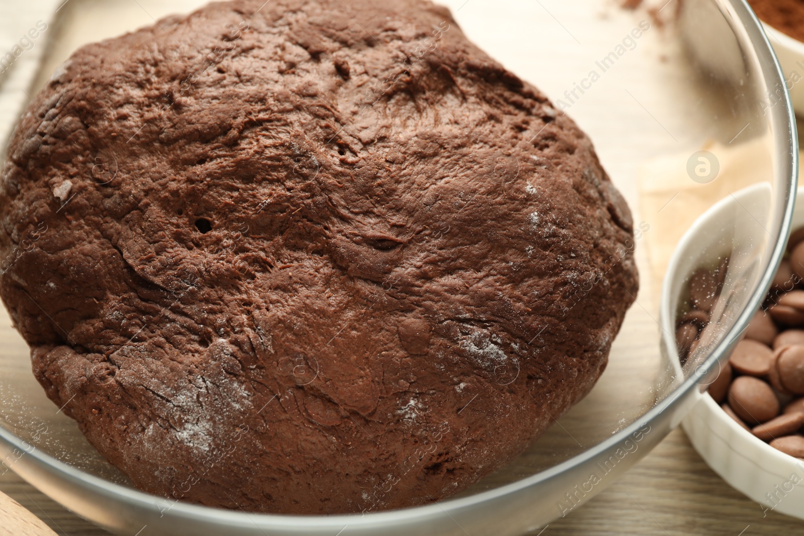 Photo of Chocolate dough in bowl on wooden table, closeup