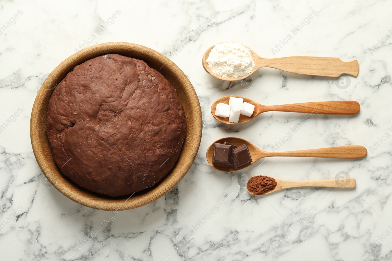 Photo of Chocolate dough and ingredients in spoons on white marble table, flat lay