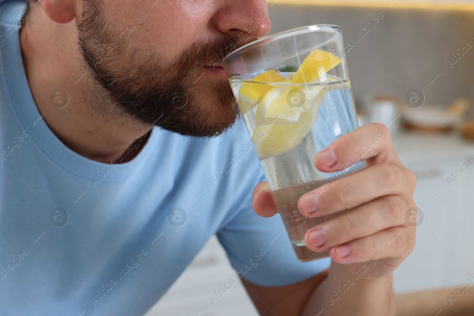 Photo of Man drinking water with lemon indoors, closeup