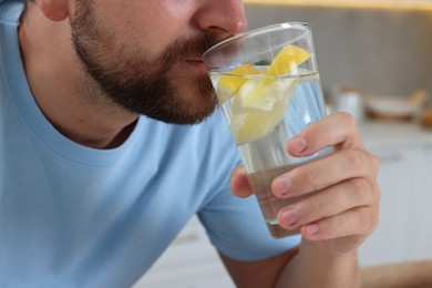 Man drinking water with lemon indoors, closeup