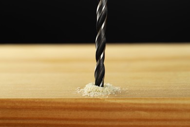 Photo of Drilling hole in wooden plank on black background, closeup