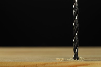 Photo of Drilling hole in wooden plank on black background, closeup. Space for text