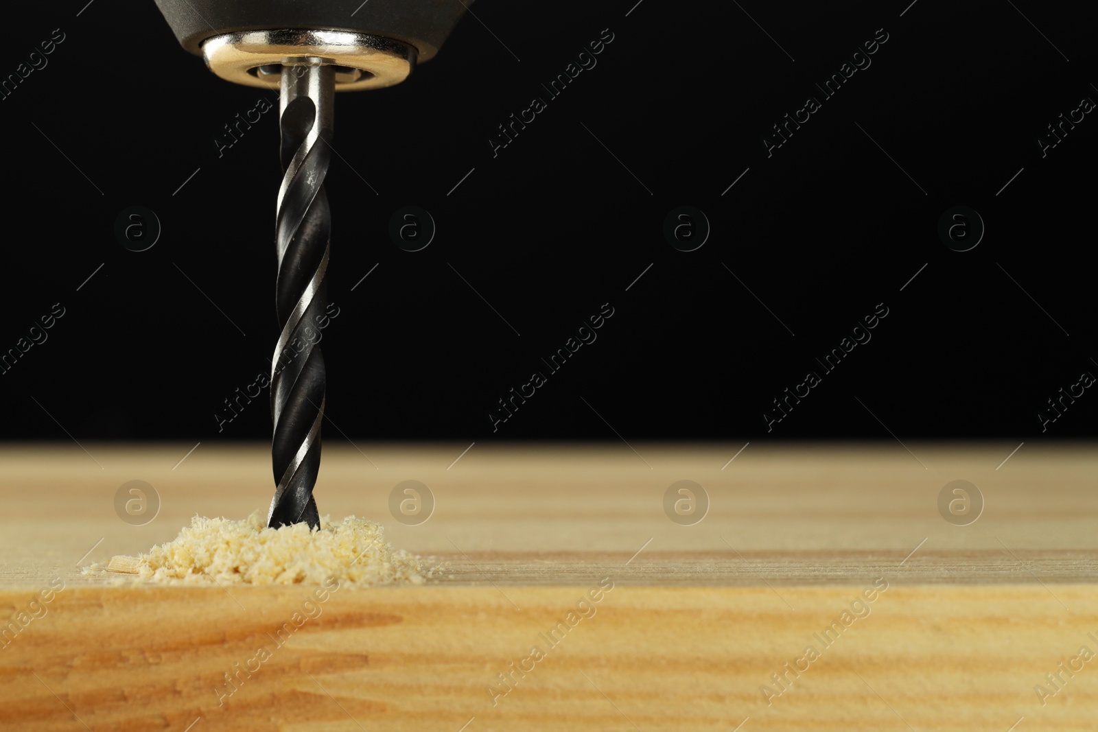 Photo of Drilling hole in wooden plank on black background, closeup. Space for text