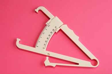 Plastic body fat caliper on pink background, top view