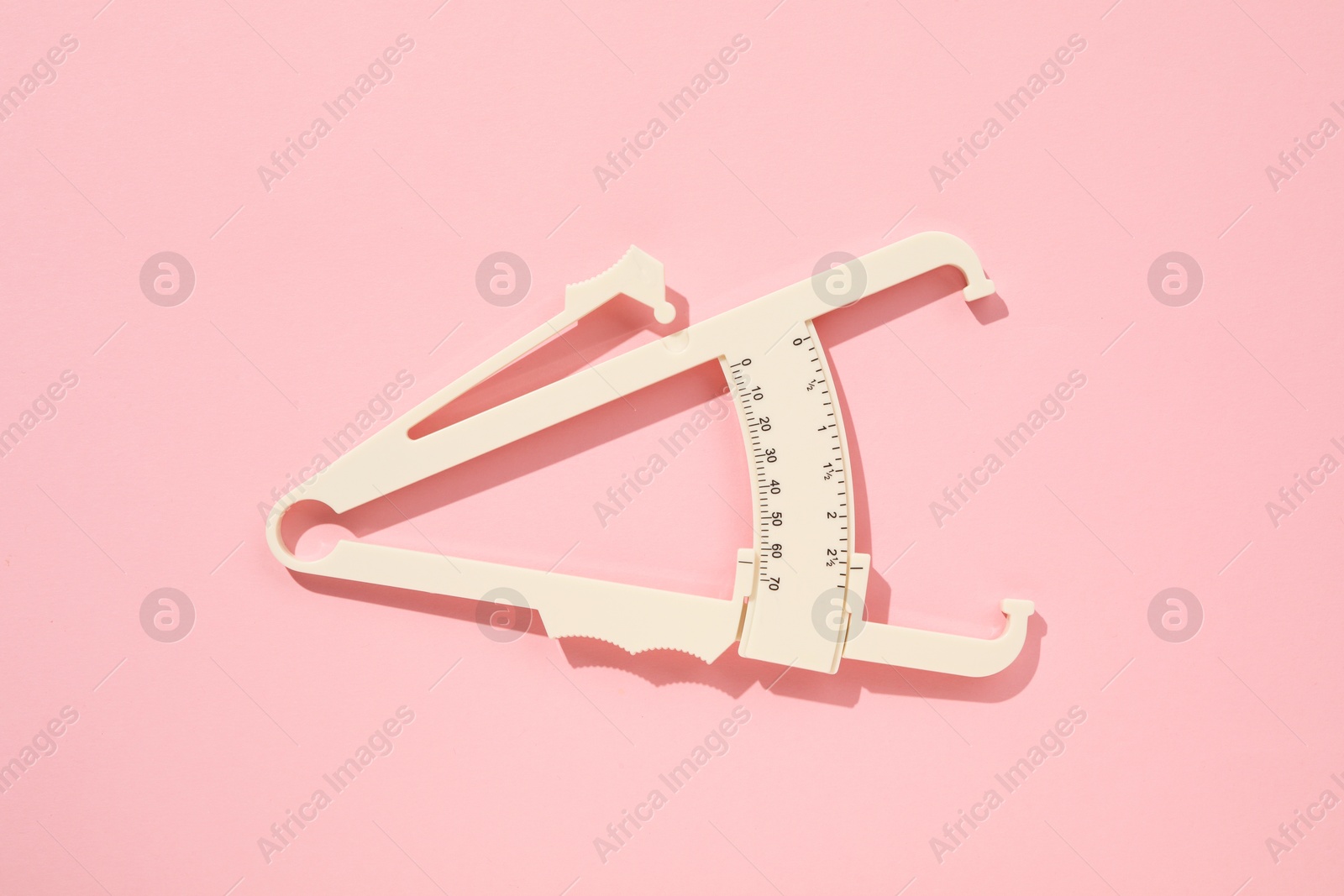 Photo of Plastic body fat caliper on pink background, top view