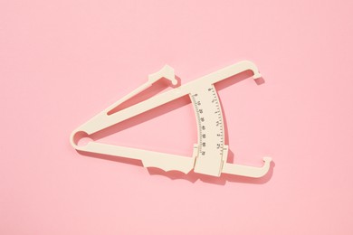 Photo of Plastic body fat caliper on pink background, top view