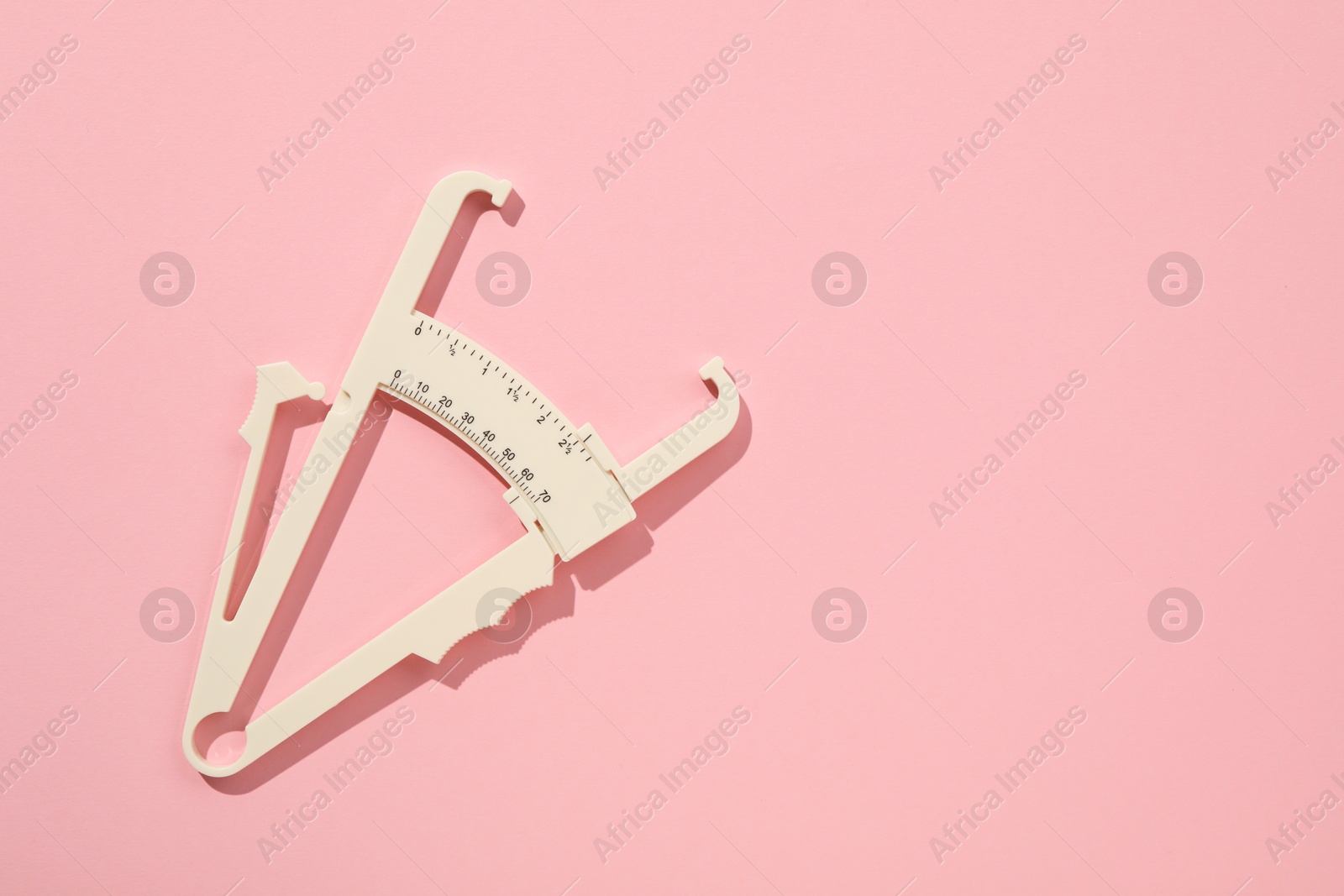 Photo of Plastic body fat caliper on pink background, top view. Space for text