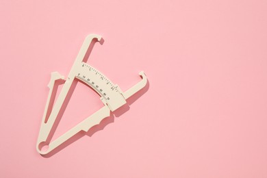 Plastic body fat caliper on pink background, top view. Space for text