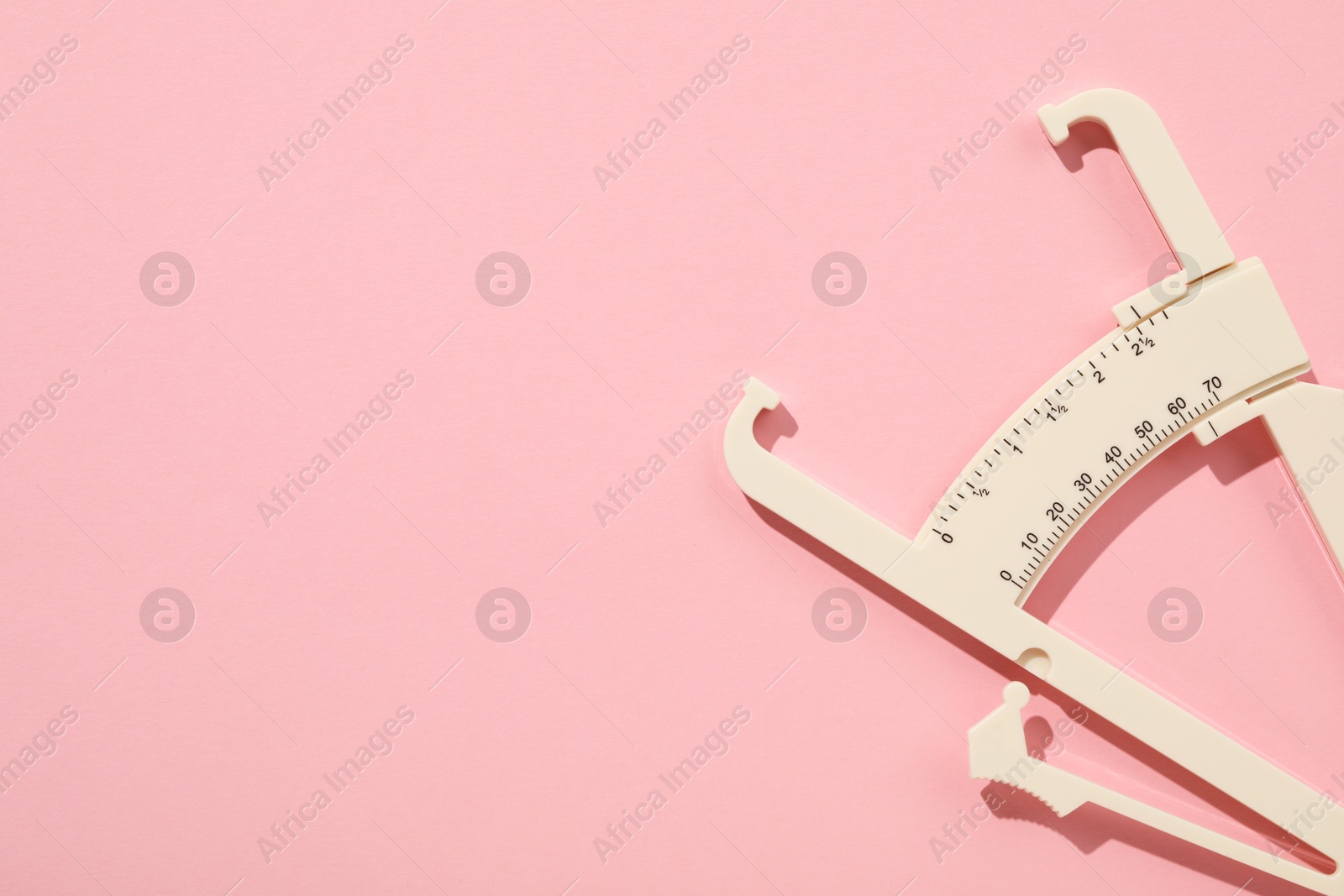 Photo of Plastic body fat caliper on pink background, top view. Space for text