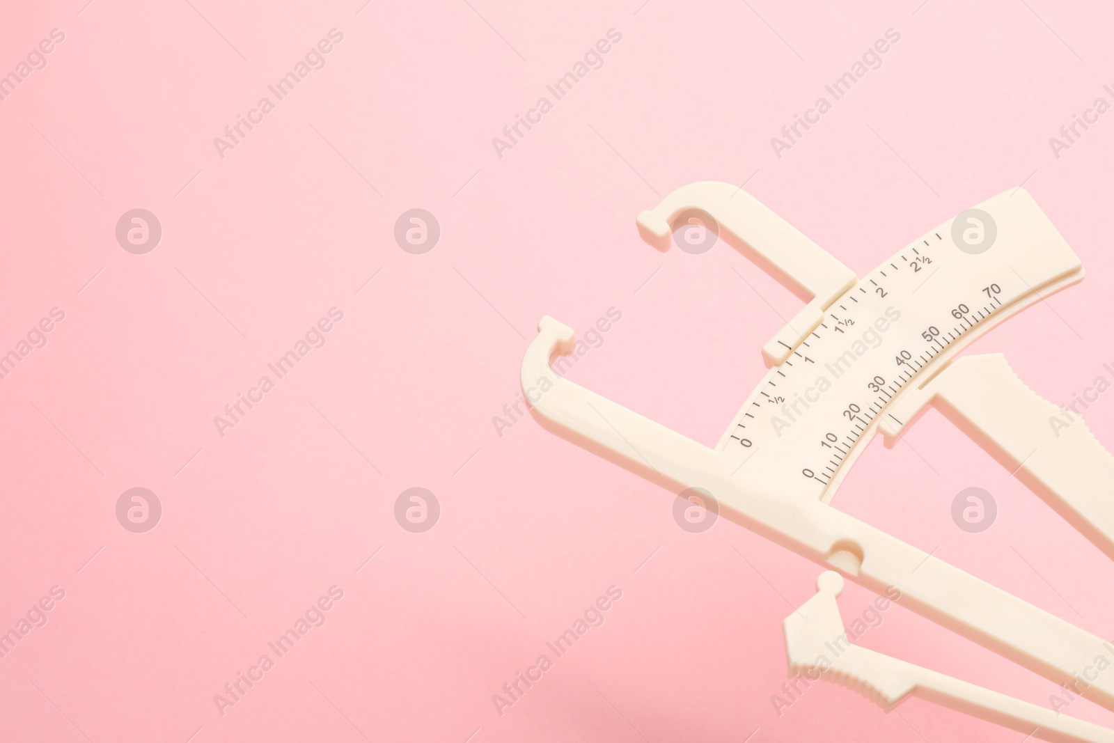 Photo of Plastic body fat caliper on pink background, closeup. Space for text