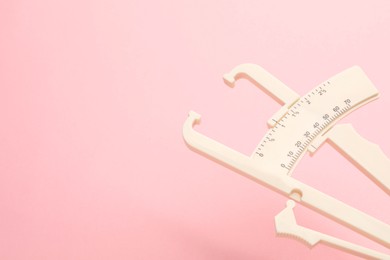 Plastic body fat caliper on pink background, closeup. Space for text