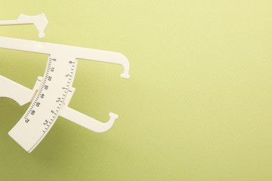 Photo of Plastic body fat caliper on light green background. Space for text