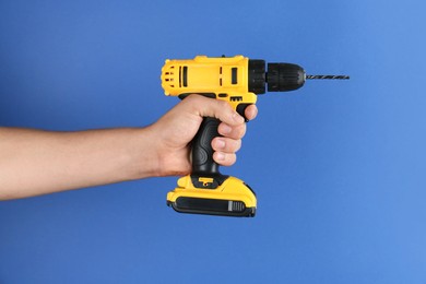 Photo of Man with cordless electric drill on blue background, closeup