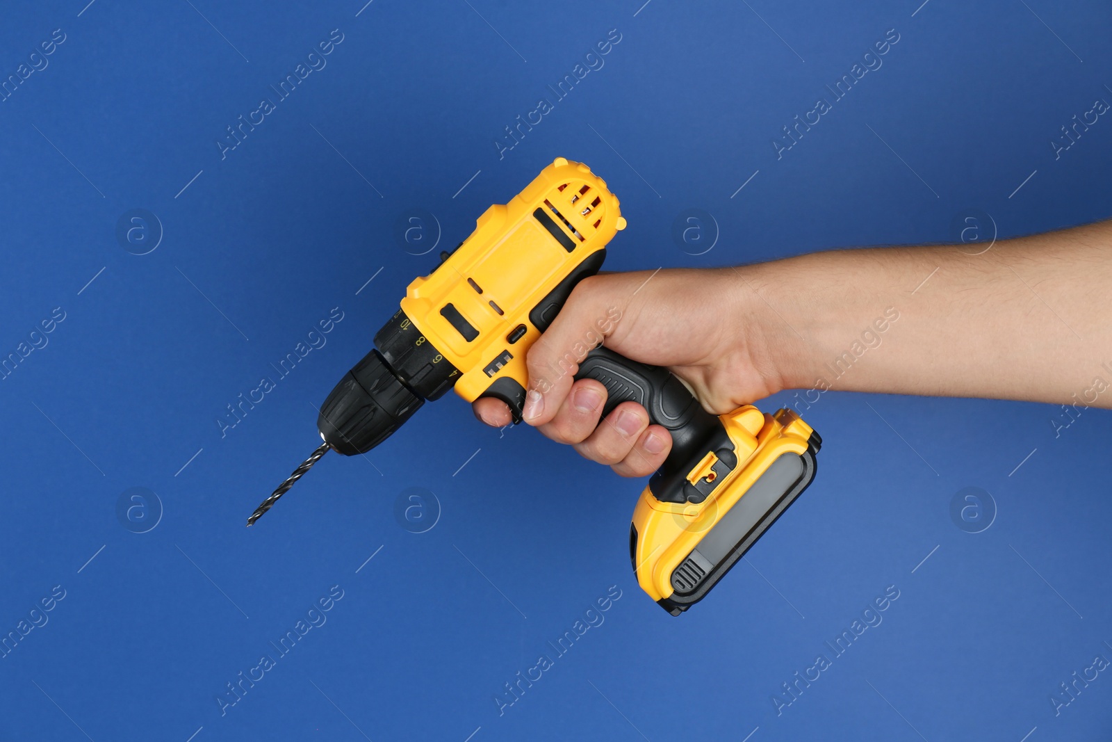 Photo of Man with cordless electric drill on blue background, closeup