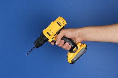 Photo of Man with cordless electric drill on blue background, closeup