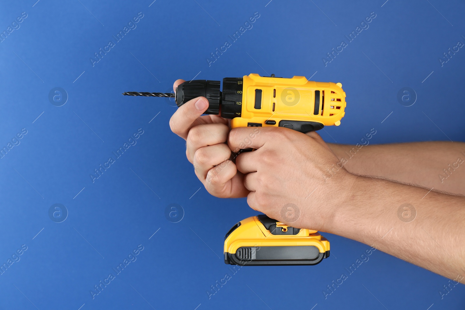 Photo of Man with cordless electric drill on blue background, closeup