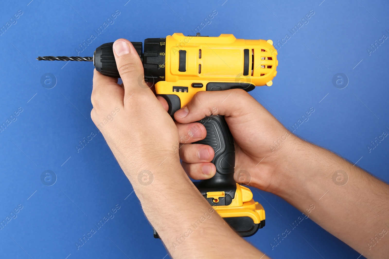 Photo of Man with cordless electric drill on blue background, closeup