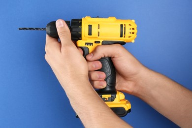 Photo of Man with cordless electric drill on blue background, closeup