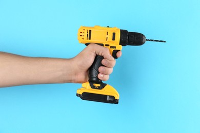 Photo of Man with cordless electric drill on light blue background, closeup