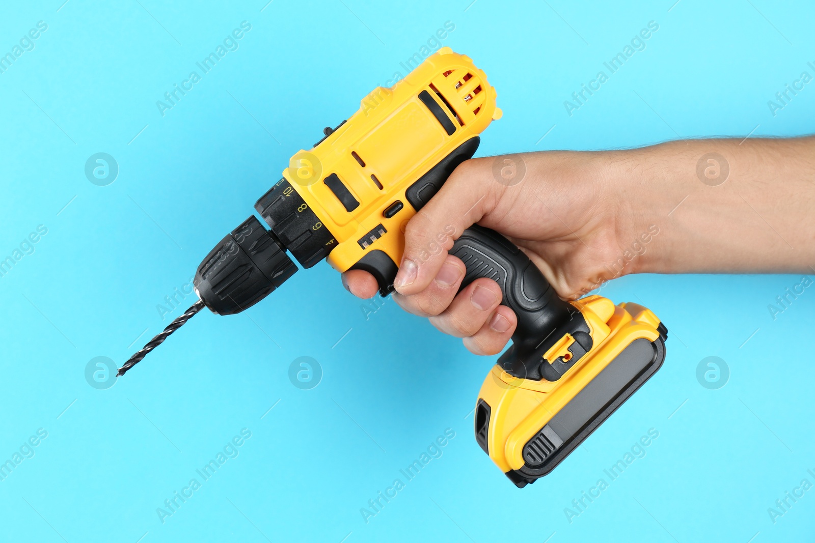 Photo of Man with cordless electric drill on light blue background, closeup