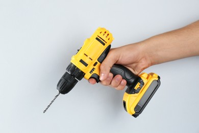 Photo of Man with cordless electric drill on light grey background, closeup