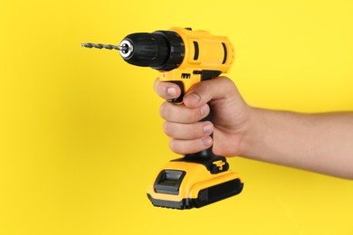 Photo of Man with cordless electric drill on yellow background, closeup