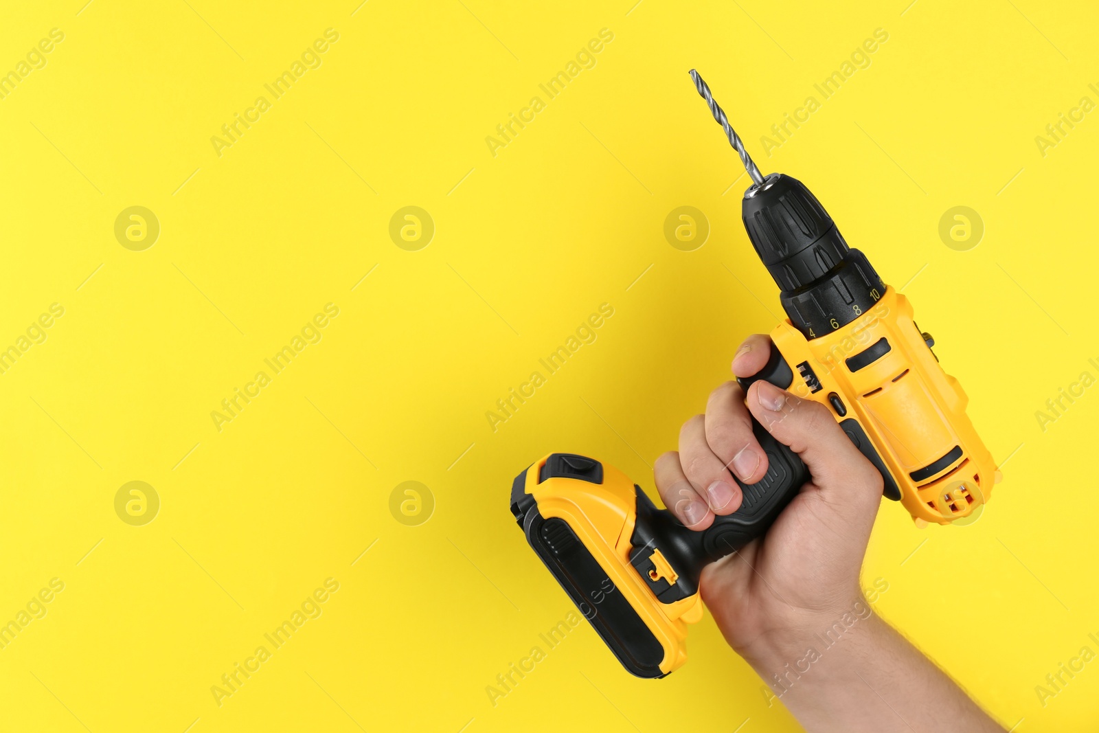 Photo of Man with cordless electric drill on yellow background, closeup. Space for text