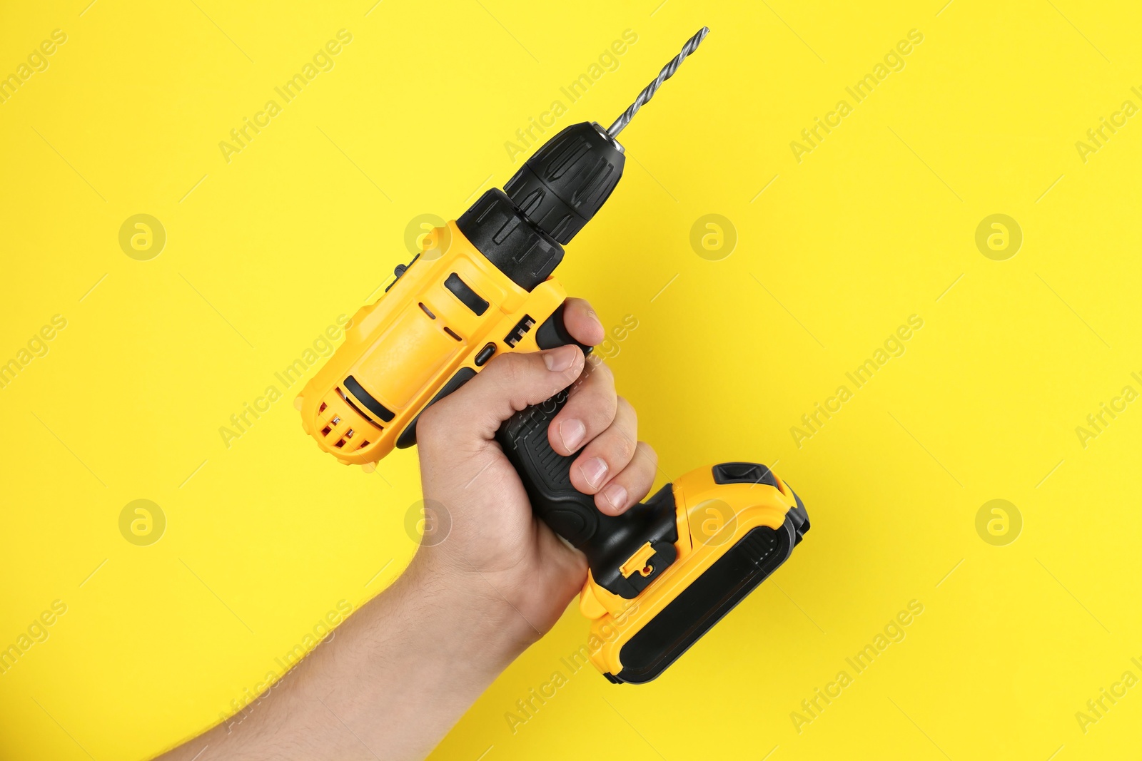 Photo of Man with cordless electric drill on yellow background, closeup