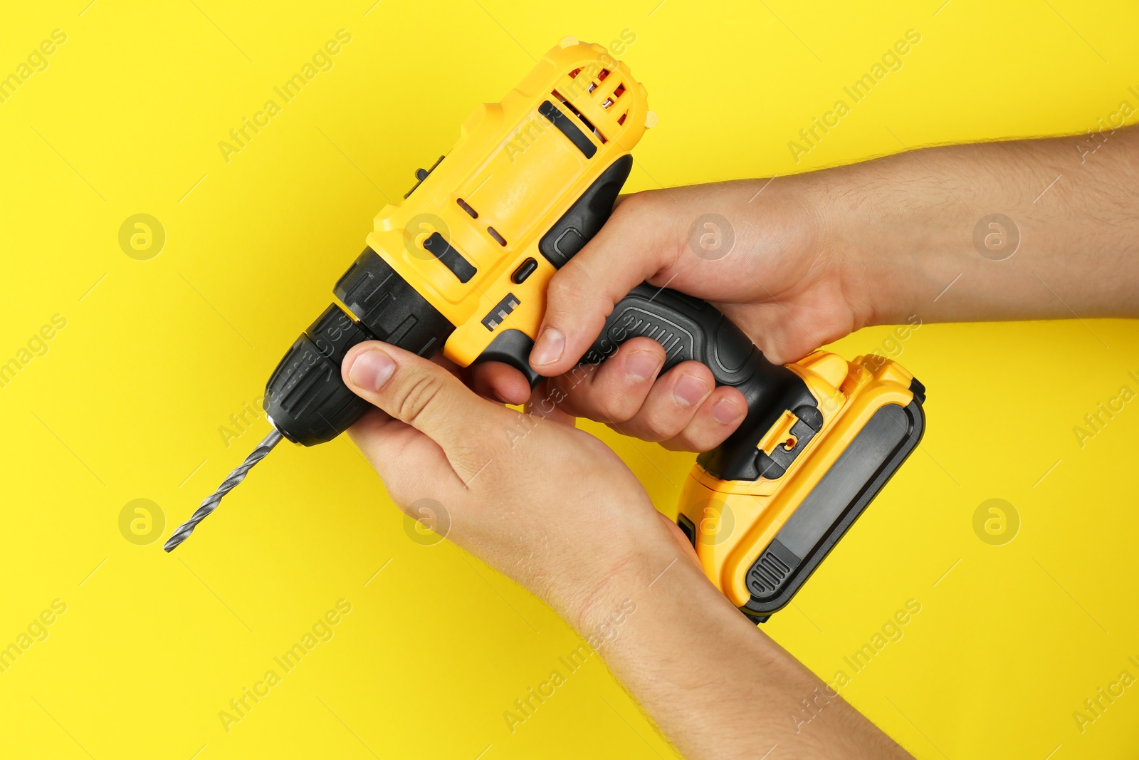 Photo of Man with cordless electric drill on yellow background, closeup