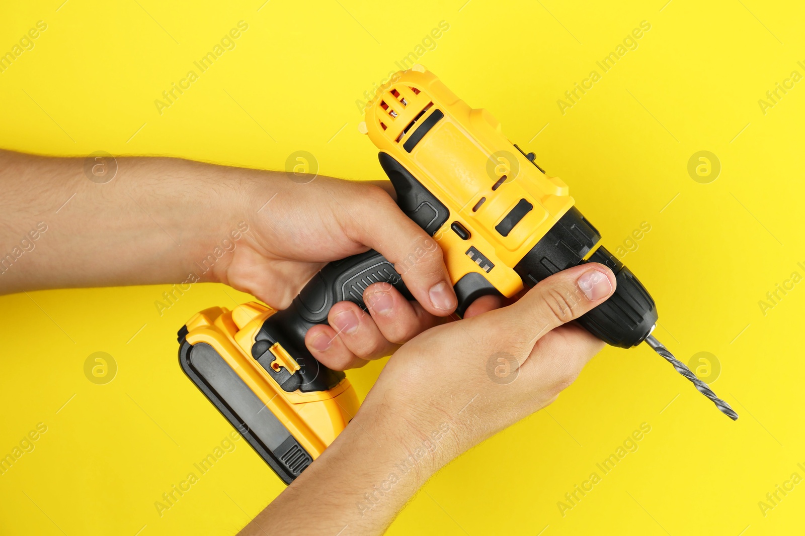 Photo of Man with cordless electric drill on yellow background, closeup