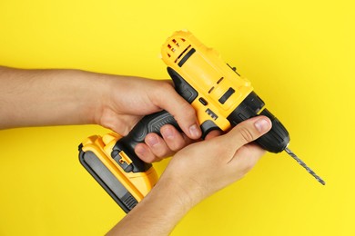 Man with cordless electric drill on yellow background, closeup