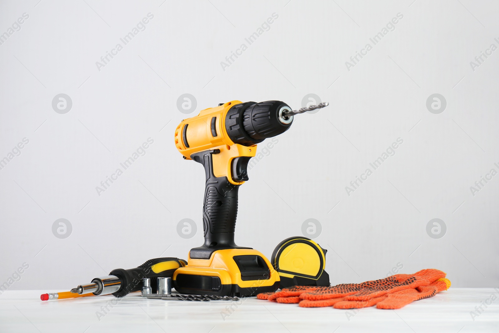 Photo of Cordless electric drill, gloves, bits, screwdriver and measuring tape on white wooden table